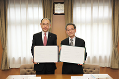 協定書を掲げる古山学長（右）と西尾社長