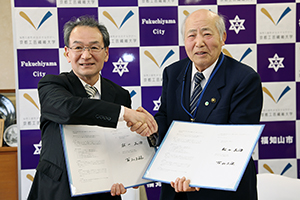 協定書を掲げる古山学長・松山正治福知山市長