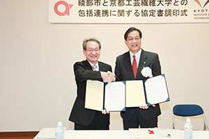 協定書調印式にて山崎善也綾部市長と握手を交わす古山学長（写真左）