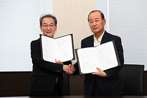 協定書を掲げる古山正雄学長と松田憲二代表取締役社長